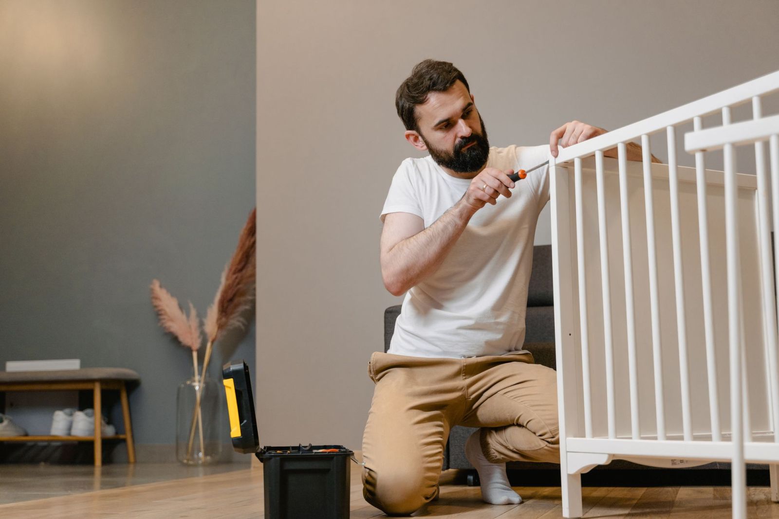 A man assembling a white wooden cot with a screwdriver