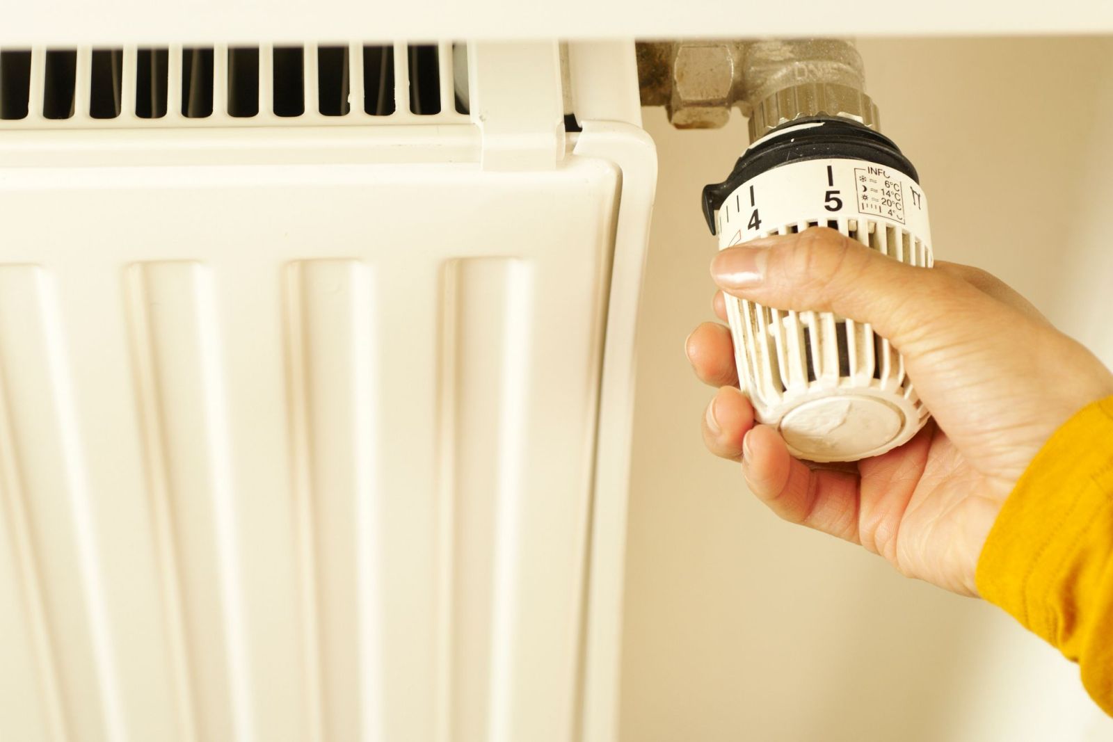 A hand turning the thermostat valve on a radiator