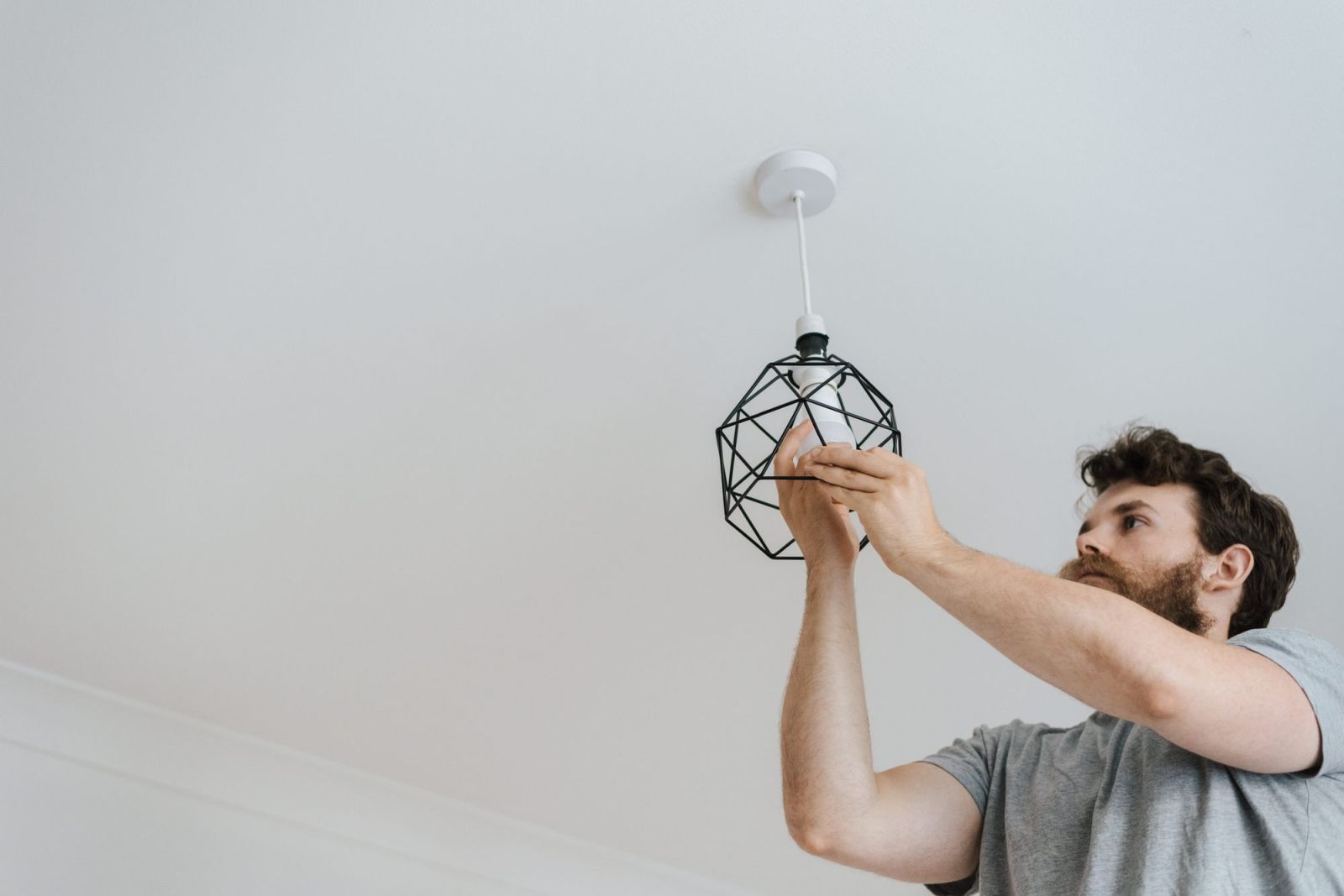 A man fitting a pendant light to a ceiling