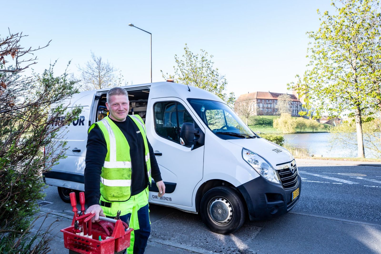 A tradesman in a high-visibility jacket carrying his toolbox from a white van